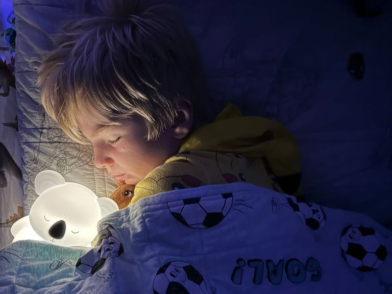Child lying in bed with a koala bear night light and soccer-themed blanket