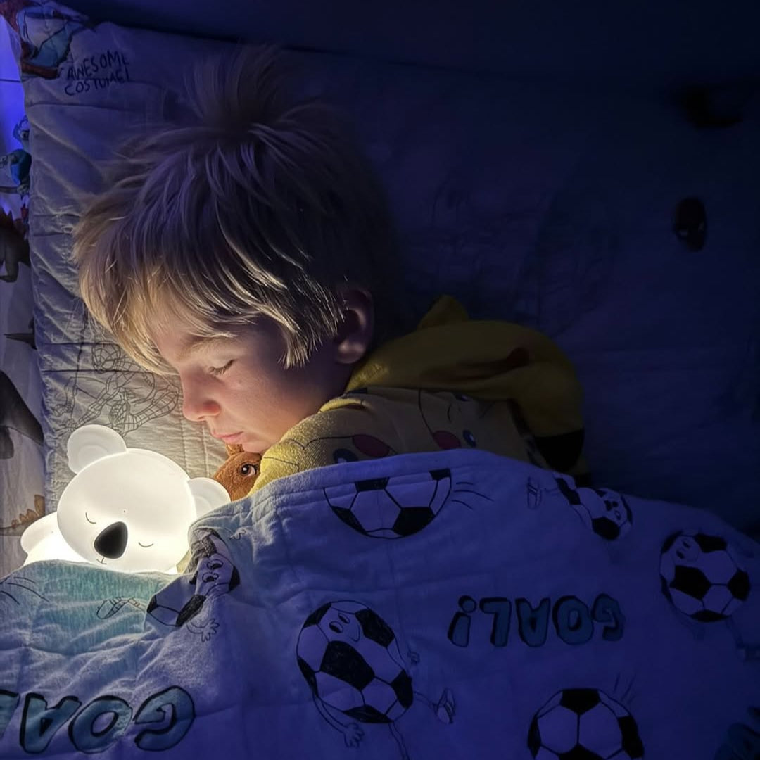 Child lying in bed with a koala bear night light and soccer-themed blanket